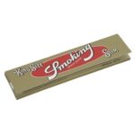 En pakke med cigaretpapir præsenterer sig i en elegant, gylden farve. Forsiden er prydet med en sort og hvid tekst, der angiver produktets navn og type. Papiret er slim og king size, hvilket fremgår af de tydelige skrifttyper. Den glatte overflade reflekterer lys, mens kanterne er skarpe og præcise. Pakken har en praktisk lukning i toppen.