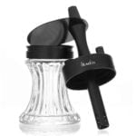 En sort, bærbar vandpibe med en glat, cylindrisk krop. Den har en metalbund og en transparent slange, der buer elegant. Øverst er en skål med et fint gittermønster, der holder tobaksblandingen. Håndtaget er ergonomisk formet, og der er en silikonebelægning, der sikrer et godt greb. Den samlede struktur er kompakt og praktisk.