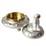 En askeholder i form af et rumskib præsenteres med en glat, metalisk overflade i sølv og grå nuancer. Rumskibets design inkluderer detaljerede vinduer og motorer, der er skabt med præcise linjer. Der er en åben sektion til opbevaring af aske, mens bunden har en flad, stabil overflade, der sikrer, at den står sikkert.