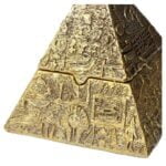 Et askebæger i form af en pyramide præsenteres med en glat, sort overflade. De tre synlige sider er lige, og toppen er flad med en lille åbning i midten. Bunden er stabil og bredere end sideskæringerne, hvilket giver en sikker placering. Materialet ser ud til at være keramik eller metal med en blank finish, der reflekterer lys.