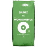 Mørkebrunt, granuleret materiale fylder en stor, transparent plastikpose. Overfladen er ujævn med små klumper, der skaber en grov tekstur. Posen er lukket med en sort zip-lukning, og der er et farvetiket på forsiden med grønne og blå nuancer. Baggrunden er neutral, hvilket fremhæver posens indhold.