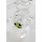 En sort bongs struktur er præget af glatte, buede former og en høj, slank hals. Materialet er gennemsigtigt, hvilket afslører en indvendig perkolator med små bobler, der skaber et visuelt spil. Bunden er bred og stabil, mens en afrundet, sort bladformet dekoration pryder siden. Kanten af mundstykket er let afrundet for komfort.