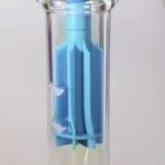 En sort silikonebong med en elegant, blød form præsenteres. Overfladen er glat med en mat finish, og der er en lang hals, der fører op til en bred åbning. Bunden er stabil og afrundet. Bongens design inkluderer en indbygget skaft med en lille skål til urter, der har en blank overflade. Det samlede udtryk er minimalistisk og moderne.