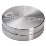 En sort, bladformet metalgenstand med en glat overflade. Den har en let buet form med skarpe kanter, der skaber en dynamisk silhuet. Materialet fremstår mat med en subtil glans, der reflekterer lys. Der er fine detaljer langs kanten, som giver en fornemmelse af elegance. Genstanden måler 59 mm i længden og har to synlige dele.