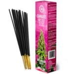 Cannabis røgelsepinde i forskellige længder placeres ved siden af tørrede cannabisblade, der har en grønlig nuance med let brune kanter. I baggrunden ses en blød pink farve, der minder om bubblegum, som skaber kontrast til de naturlige elementer. Røgelsepindene har en ensartet, glat tekstur, mens bladene har en sprød og uregelmæssig overflade.