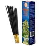 Cannabis røgelsespinde præsenteres i en bund af tørrede cannabisblade, der har en grønlig-brun farve og en delikat struktur. Røgelsespindene er slanke og cylindrisk formede, med en mørkebrun farve. Nag Champa, der er synlig på emballagen, indeholder gyldne og hvide nuancer, samt tekst i en elegant skrifttype. Elementerne er arrangeret harmonisk, hvilket skaber en visuel balance.