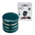 En porcelæns kværn i en dyb grøn farve præsenterer sig med en glat og skinnende overflade. Den har en cylindrisk form med en diameter på 63 mm. Øverst findes en metalknap, der fremstår i kontrast til det glatte porcelæn. Kværnen har en fin struktur, der tilføjer et elegant touch, og det samlede design udstråler en enkel, moderne æstetik.