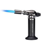 En sølvfarvet gaslighter med en glat, metaloverflade, der har en let reflekterende kvalitet. Den har en buet form og en ergonomisk håndtag, der afsluttes med en justerbar flammeåbning. Knapperne er sorte og placeret på siden, hvilket giver en kontrast til det metalliske udseende. Lighterens design er enkelt og funktionelt med tydelige linjer.