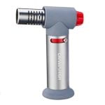 En høj, slank lighter i metal med en sølvfarvet overflade prydet af blå flammer. Lighterens krop har en glat, reflekterende tekstur, mens den nederste del har en let buet form. Der er synlige knapper til justering af flammen, samt et lille vindue, der viser gasniveauet. Designet er moderne og strømlinet.