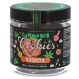 En tæt, mørkbrun blok med en glat overflade og let glans pryder den synlige flade. Strukturen er kompakt og ensartet, uden synlige sprækker. Der ses fine, lyse nuancer, der giver en let marmorering. Omkring blokken er der små krummer og partikler, der tyder på, at den er blevet brudt eller skåret.