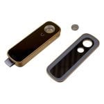En kompakt vaporizer præsenterer sig i en sort, glat plastoverflade med et minimalistisk design. Den har en tydeligt markeret skærm med digitale tal og ikoner, der angiver temperatur og batteriniveau. Knapperne er placeret på fronten, med en mat tekstur for bedre greb. En sølvfarvet kant omkranser enheden, som står på en flad, stabil base.