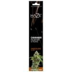 En pakke med cannabis røgelse præsenterer sig i en rektangulær, mat indpakning. Farven er en dyb grøn med nuancer af brun og guld. Et stiliseret logo pryder forsiden, omgivet af grafiske elementer, der minder om cannabisblade. Teksten er i hvid, tydelig og letlæselig. Baggrunden har en subtil tekstur, der tilføjer dybde til designet.