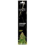 En pakke med runde, grønne og gule nuancer pryder forsiden, der præsenterer en illustration af cannabisplanter. Øverste del har en gul baggrund med teksten "Lemon Haze" i sort skrift. Nederst findes en transparent vinduesåbning, der viser de små, brune og grønne røgelsespinde indeni. Pakken har en mat overflade med en let tekstur.
