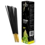 En pakke med runde kanter præsenterer en lys gul farve, dekoreret med grønne og sorte elementer. På forsiden står teksten "Lemon Haze" i en moderne skrifttype, mens baggrunden har et blødt mønster, der minder om røg. Pakken er fremstillet af pap, og der er et tydeligt fokus på naturlige og plantebaserede elementer.