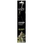 En pakke med incense har en rektangulær form og prydes af en farverig indpakning med grønne, gule og blå nuancer. Mønsteret inkluderer stiliserede cannabisblade, der er integreret i designet. Teksten er trykt i hvid og gul, med navnet "Nag Champa" fremhævet. Materialet virker glat og skinnende, hvilket skaber en iøjnefaldende effekt.