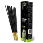 Tørrede cannabisblomster pryder en hvid ceramic skål. Blomsterne har en uregelmæssig form og varierer i størrelse, med nuancer af grøn, brun og lilla. Overfladen er tæt og dækket af fine trichomer, der glitrer i lyset. Et par blade og stilke er synlige, hvilket tilføjer tekstur til den samlede fremtoning. Skålen står på en lys overflade, der fremhæver detaljerne.