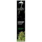 En pakke med runde kanter præsenterer et klart design i grøn og hvid. Forsiden viser et botanisk mønster, der indeholder stiliserede cannabisblade i forskellige nuancer af grøn. Øverst er teksten "Haze Cannabis Incense" i en elegant skrifttype, mens bunden bærer oplysninger i mindre skrift. Baggrunden er en lys, ensfarvet hvid, der fremhæver de grønne elementer.