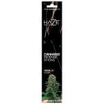 En hvid og brun emballage præsenterer et produkt med en tydelig, grafisk illustration af cannabisblade. Farverne er bløde og naturlige, med nuancer af grøn og beige. Øverst er der en sort tekst, der angiver produktnavnet, mens et logo pryder den nederste del. Emballagen er prydet med subtile detaljer, der fremhæver en organisk æstetik.