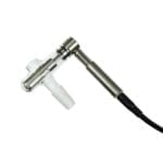 En titanium e-nail med en glat, sølvfarvet overflade pryder midten af kompositionen. Den har en cylindrisk form og er udstyret med en digital skærm, der viser temperaturindstillinger i klare, sorte tal. Kablet, der forbinder enheden, er sort og fleksibelt. Omkring e-nailen ses en transparant glasbeholder, der tilføjer en visuel kontrast til det metalliske design.