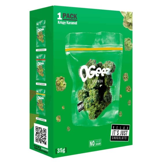 OgeeZ Krispy Karamel præsenterer sig med en gyldenbrun farve, der er glat og let skinnende. Emballagen er firkantet med afrundede hjørner og prydet med farverige grafiske elementer, herunder en tydelig sort tekst og et ikonisk logo. Overfladen har en let glinsende finish, og der er detaljerede illustrationer af ingredienserne i bunden.