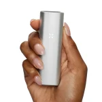 Pax Mini Vaporizer præsenterer en slank, sølvfarvet krop med en glat metaloverflade, der reflekterer lys. Den rektangulære form er strømlinet med afrundede hjørner. På forsiden findes en lille, diskret knap samt et LED-lys, der indikerer status. Det ergonomiske design inkluderer en aftagelig mundstykke i mørk plastik, der komplementerer det overordnede udseende.