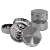 En grå metal kværn med en diameter på 63 mm. Overfladen har en børstet finish, der giver en mat tekstur. Kværnen har to sektioner med skridsikre greb på siderne og små, indgraverede tænder til formaling. Der er små huller til jævnt at fordele det malte indhold. Låget er let buet med en slank kant.