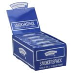 En pakke cigaretter i en dyb blå farve præsenterer sig med en glat overflade. Fronten har et stort, hvidt logo med karakteristiske skrifttyper. Pakken er rektangulær med afrundede hjørner og indeholder en lukkeåbning. På siden er der små tekstlinjer i kontrasterende farver, der beskriver produktdetaljer. Det samlede design udstråler en simpel, men iøjnefaldende æstetik.