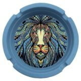 Silikoneaskebægeret har en rund form med en diameter på 80 mm. Det er præget af et detaljeret, sort-hvidt tribal løvemotiv, der viser kraftfulde linjer og geometriske mønstre. Materialet har en glat, mat overflade med en let flex, hvilket giver en blød tekstur. Askebægeret har en lav profil og en indvendig skålformet struktur.