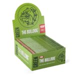 En boks præsenterer sig med en rektangulær form i en dyb grøn farve. Designet inkluderer en illustration af en bulldog med detaljerede linjer og en tekst i hvid, der angiver produktets navn. Boksens overflade har en mat finish, mens kanten er let afrundet. Indholdet indikeres som king size slim papir, hvilket antyder en smal og lang form.