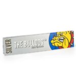 En sølvfarvet tobaksrullepapir pakke præsenterer sig med en slank, rektangulær form. Forsiden prydes af en sort og hvid logo med en stiliseret hund. Teksten "King Size Slim" er tydeligt trykt i en moderne skrifttype, mens baggrunden har en glat, metallisk finish. Pakken har en lukning med en let tilgængelig flap, der sikrer indholdet.