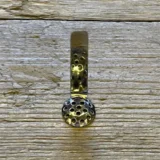 En 15 mm bred rist lavet af rustfrit stål pryder overfladen med en glat, reflekterende tekstur. Risten har et geometrisk mønster bestående af jævnt fordelte, små åbninger, der skaber en visuel rytme. Kanterne er præcist skåret, hvilket giver en skarp, moderne finish. Den har en silvery metallic farve, der fremhæver materialets holdbarhed.