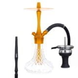En gylden lampe i en klassisk, orientalsk stil pryder overfladen. Lampen har en buet, skulpturel form med detaljeret mønstring, der skaber et indviklet lys- og skygge-spil. Den er fremstillet af metal med en blank overflade, der reflekterer lys. En fin, dekorativ krone afslutter toppen, mens en lampefod i samme stil giver stabilitet.