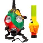 En gasmaske med et rasta-inspireret design pryder en bongs struktur. Farverne rød, grøn og gul skaber et livligt mønster, mens den sorte silikonebase giver en mat overflade. Maskens linser er klare og runde, omkranset af en robust ramme. Bongen har en glat, gennemsigtig krop og en krum hals, der fører til en bred åbning.