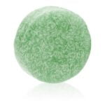 En solid shampoo i form af en rund skive, der vejer 60 gram. Overfladen er jævn og har en let glat tekstur, mens farven varierer fra en lys grøn til en dybere grøn nuance. Der er en subtil marmorering, der tilføjer et naturligt udseende. Ingen synlige indpakninger eller etiketter pryder produktet.