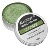En solid shampoo i form af en rund skive med en glat, ensartet overflade. Farven er en dyb grøn, der minder om naturens nuancer. Overfladen har en let mat finish med små, fine teksturer. Der er ingen synlige emballageelementer, og skiven ligger fladt på en neutral baggrund, hvilket fremhæver dens farve og form.