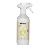 En transparent flaske med en grøn spraydysse står centralt. Flasken indeholder en lysebrun væske og har en etiket med grøn og hvid tekst, der angiver produktinformation. Etiketdesignet inkluderer en stiliseret plante og en grå baggrund med teksturer. Flaskens form er cylindrisk og slank, og spraydysen er rund med en let buet spids.