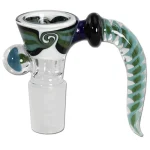 En skål fremstillet af klart glas pryder en dyb sort farve, som danner en kontrast til en grøn spiral, der elegant snor sig indad. Skålens kant er let bølget, hvilket tilføjer en organisk form til designet. Overfladen har en glat, skinnende tekstur, der reflekterer lys og fremhæver de farverige detaljer i mønsteret.
