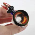 En dyb skål med en elegant, sort glasoverflade, der reflekterer lys og skaber en glinsende effekt. Skålen har en asymmetrisk form med bølgende kanter, der minder om blade. Indersiden prydes af en swirl-mønster i nuancer af grå og hvid, hvilket tilføjer dybde og tekstur. Materialet fremstår glat og poleret, hvilket understreger håndværkets kvalitet.