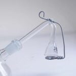 En sort glas bongadapter med en glat overflade, der reflekterer lys. Adapterens form er cylindrisk med en smal hals og en bredere base, hvilket sikrer stabilitet. Den har et SG 14 tilslutningspunkt, der er markeret med en tydelig kant. Materialet er transparent i bunden, hvilket giver et indblik i den indre struktur.