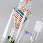En sort bong med en bladformet dekoration, fremstillet af glas. Den har en glat overflade med en dyb, mørk farve og en lilla detalje i halsen. Bongen har en buet form, der giver et elegant udtryk. Den er udstyret med en skål til brug af urter og en vandkammer nederst, hvilket skaber en funktionel og æstetisk enhed.