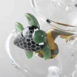 En sort percolator olie-rig i form af en skildpadde med detaljerede blade på skildpaddens ryg. Den har en glat, blank overflade og er lavet af glas, hvilket giver et elegant udseende. Riggen måler 19 cm i højden og har flere rør og en percolator, der skaber bobler, når væske passerer gennem. Elementerne er omhyggeligt placeret for maksimal funktionalitet.