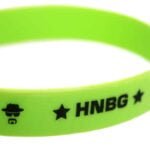 Et armbånd i en dyb grøn farve, fremstillet af elastisk materiale, der giver en glat og blød overflade. Armbåndet prydes af en diskret, sølvfarvet metalplade med inskriptionen "Heisenberg". Pladen har en blank finish, der reflekterer lys. Designet er enkelt og stilrent, med en ensartet tykkelse gennem hele armbåndet.