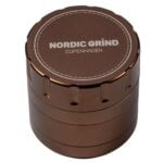 En skive i bronze med en diameter på 60 mm præsenterer en glat, poleret overflade, der reflekterer lys og skaber bløde skygger. Kanten er let afrundet, hvilket giver en blødere silhuet. Mønstrene på overfladen er subtile og tilfører dybde, mens en lille, indgravet tekst i midten tilføjer detaljer. Farven spænder fra gyldent til dybt bronze.