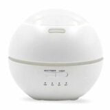 En hvid, kuppelformet beholder med en glat, skinnende overflade pryder midten af kompositionen. Den runde base er stabil og flad, mens den kuplede del har en let gennemsigtig struktur, der skaber en illusion af luftighed. Omkring beholderen er der en subtil refleksion, der fremhæver dens elegante form og enkle design, der udstråler minimalisme.