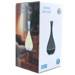 En aromadiffuser med en cylindrisk form i lyst træ, der har en glat overflade. Den øverste del er gennemsigtig, hvilket afslører en indvendig beholder til vand og æteriske olier. En USB-port er placeret i bunden, og der er en enkelt knap til betjening. Diffuseren udsender blødt lys i nuancer af hvid og blå, der skaber en beroligende atmosfære.