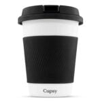 En sort kaffekop med en glat, blank overflade pryder midten af beskrivelsen. Koppen har en rund krop med en bred åbning og en tydelig, opadbuet kant. På siden ses en integreret håndtag med en let buet form. Indvendigt er koppen lysere, hvilket skaber en kontrast til den mørke yderside. Formen er organisk og harmonisk.