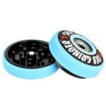 En grinder med en diameter på 57 mm præsenterer sig i en dyb blå farve. Overfladen har en glat, metalagtig tekstur og er prydet med et stiliseret design af en skater på toppen. Elementerne er skarpt definerede med tydelige kanter, og der er små, perforerede huller i bunden, der muliggør en effektiv møllefunktion.