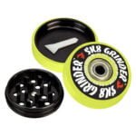 En grøn grinder med en glat overflade fremstår i en skarp neonfarve. Den har en cirkulær form med en diameter på 57 mm og er opdelt i to sektioner. Indersiden rummer skarpe tænder til formaling, mens den ydre kant har en let skridsikker tekstur. Et lille, afrundet håndtag er placeret på toppen for nem åbning.