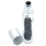 En sort rollerflaske i glas har en glat overflade med en dyb, ensartet sort farve. Flasken har en rund form med en bred bund og en smal hals, der afsluttes med en rullende applikator. Rulleren er lavet af metal, og der er en skruehætte, der sikrer tæthed. Flaskens minimalistiske design fremhæver elegance og funktionalitet.