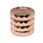 En kaffekværn præsenterer sig med en glansfuld rosegold finish. Den cylindriske form afsluttes med en sort, flad top og en fintmasket kværn indeni. På fronten ses en lille, rund knap i sort, mens den nederste del har en transparent beholder til det malede kaffe. Overfladen er glat med lette refleksioner fra lyset.